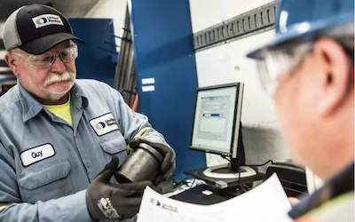 two workers discussing an equipment part at a counter