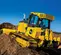 Yellow John Deere 110 HP bulldozer moving dirt up an incline with a worker in the cab