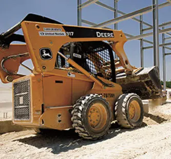 yellow john deere skid steer on jobsite in front of framed building
